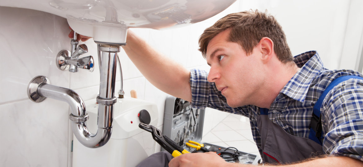 Young plumber fixing a sink in bathroom